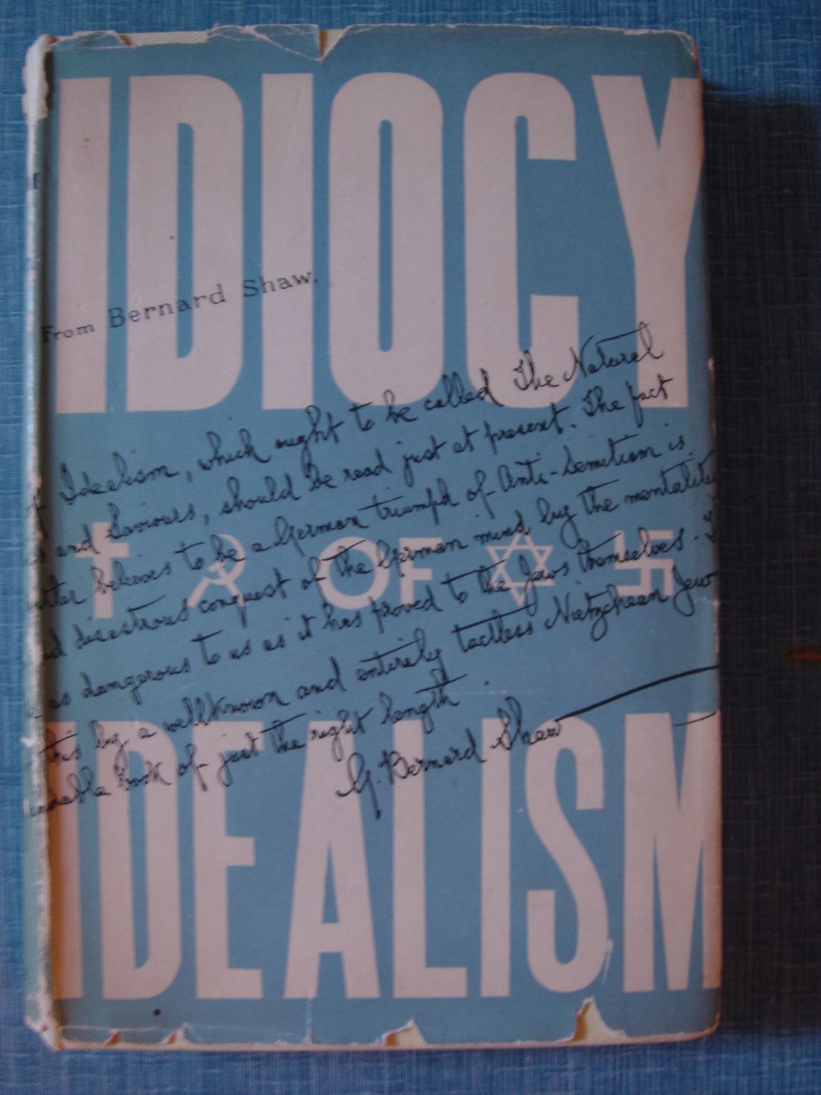 <p>Oscar Levy: <em>The Idiocy of Idealism.</em> London, Edinburgh, Glasgow (William Hodge and Company) 1940. Originalschutzumschlag mit Kreuz, Hammer und Sichel, Davidsstern und Hakenkreuz sowie Zitat von George Bernard Shaw in dessen Handschrift.</p>
